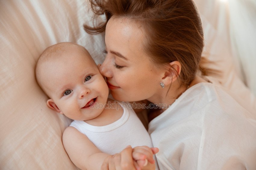 Happy young mother with baby white room mom are lying kissing baby