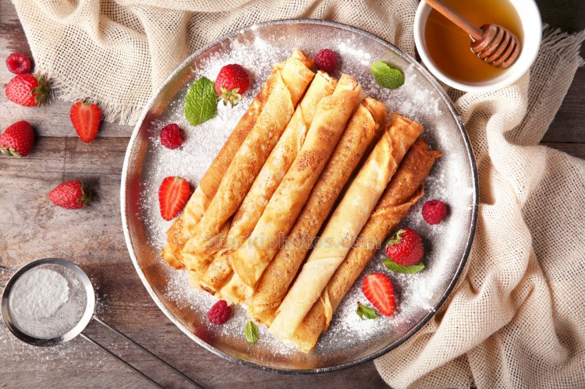 Metal plate with delicious thin pancakes on kitchen table