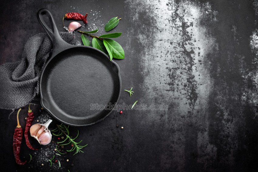 cast iron pan and spices on black metal culinary background, view from above