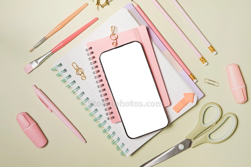 Mobile phone and pink school supplies on a green background. Back to school. Flat lay, top view.