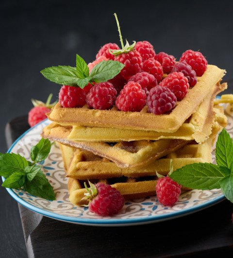 Stack of baked Belgian waffles with ripe red raspberry, green mi